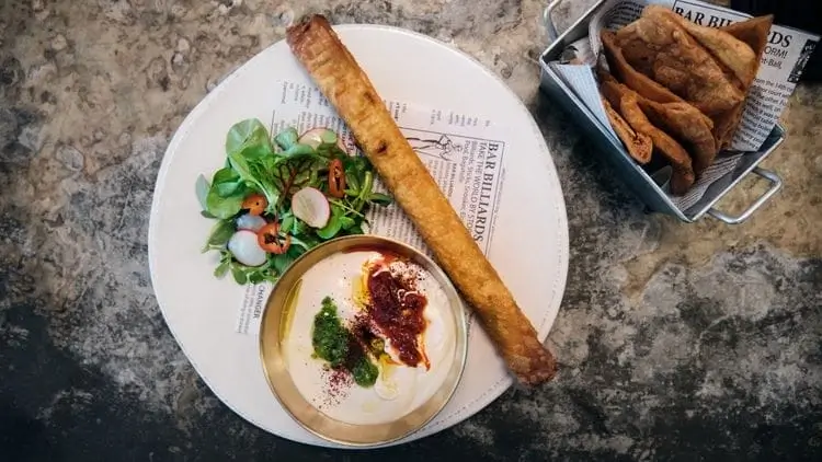 there is a plate of food with a roll and a bowl of dip