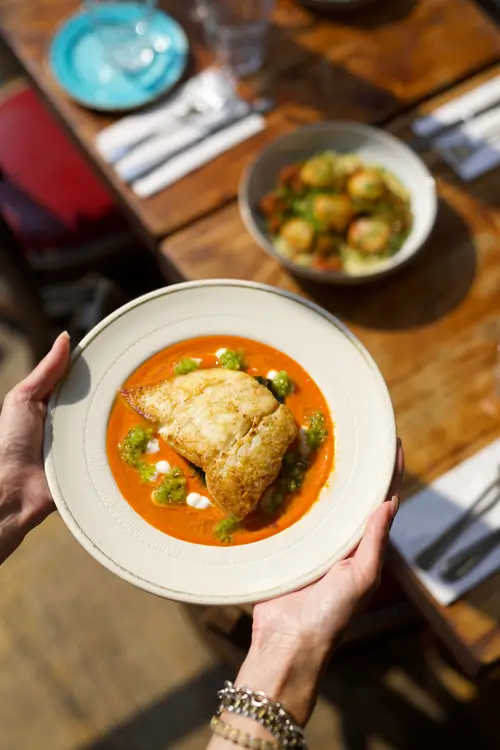 someone holding a plate of food with a fish dish on it