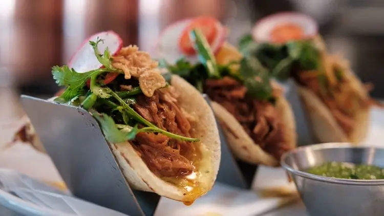 there are three tacos on a plate with a small bowl of salsa