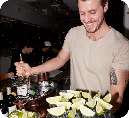 arafed man in a bar preparing a drink with limes and a cigarette