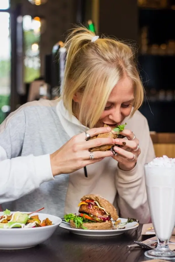 blonde woman eating a sandwich and drinking milkshake at a restaurant