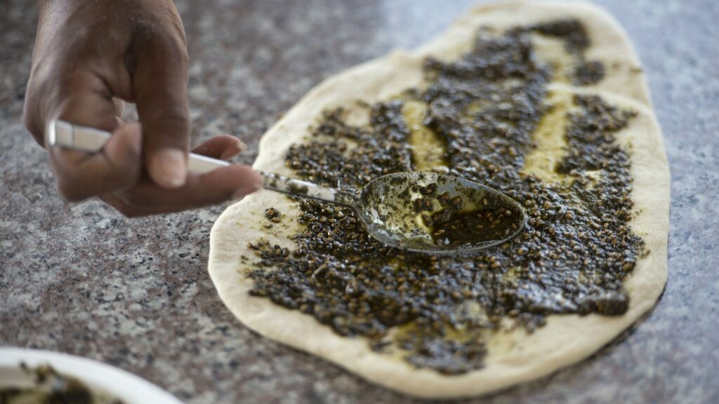 someone is making a pizza with a spoon and a bowl of sauce